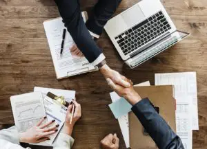 Home buyers and their Realtor shaking hands over a table covered with paperwork.