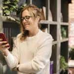 A woman looking at her phone while trying to buy a house remotely.